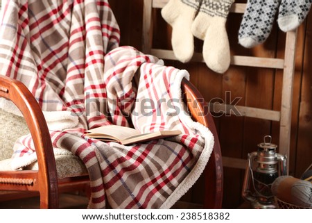 Rocking chair with plaid and book near wooden wall
