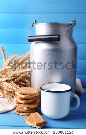 Retro can for milk, milk in cup, cookie and sheaf on color wooden background
