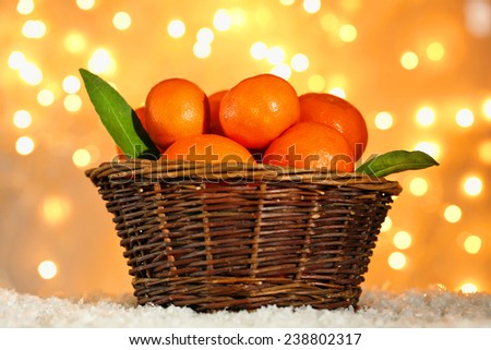 Fresh ripe mandarins in wicker basket, on snow, on lights background