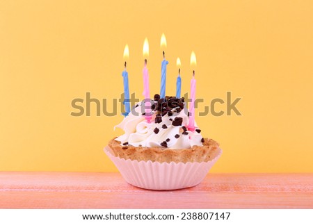 Birthday cup cake with candles on color wooden table and orange background