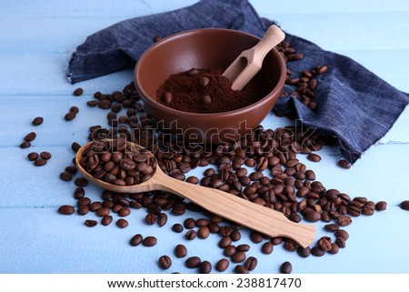 Brown bowl of ground coffee and coffee beans with wooden spoon and scoop on blue wooden background with jeans material