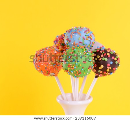Sweet cake pops in vase on yellow background