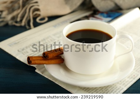 Cup of coffee with newspaper, plaid and cinnamon on color wooden background