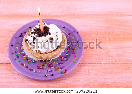Birthday cup cake with candles and sparkles on plate on color wooden background