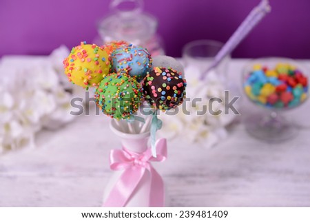 Sweet cake pops in vase on table on purple background
