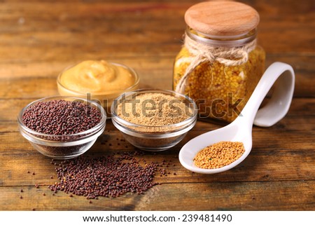 Mustard seeds, powder and sauce in glass jar, bowls and spoon on wooden background