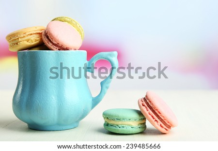 Assortment of gentle colorful macaroons in colorful mug on color wooden table, on light background