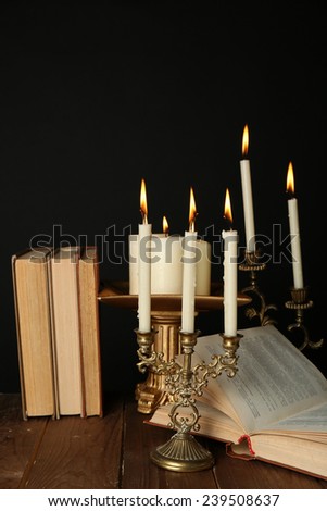 Retro candlesticks with candles and books, on wooden table, on black background