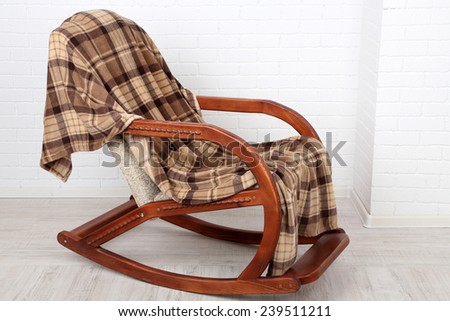 Rocking chair covered with plaid on wooden floor near the brick wall background