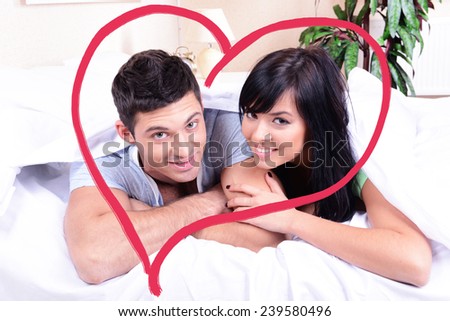 Beautiful loving couple lying in bed and heart-shaped frame