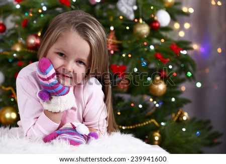 Little girl with mittens lying on fur carpet on Christmas tree background