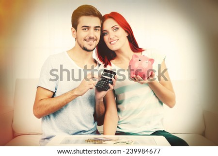 Loving couple sitting in sofa with piggy bank in room