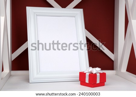 Photo frame with present box on shelf, on color wall background