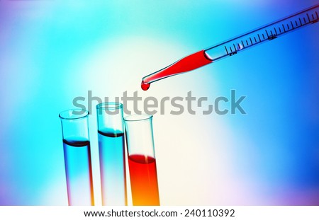 Pipette adding red fluid to the one of test-tubes on light background