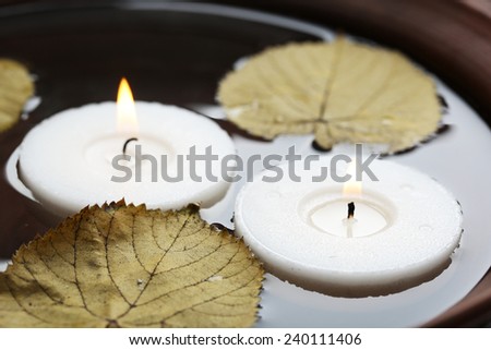 Two white candles floating with leaves on water in bowl