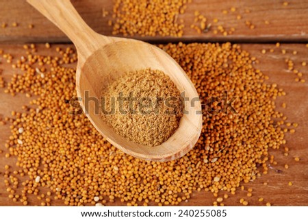 Mustard powder in wooden spoon on mustard seeds, on  wooden background