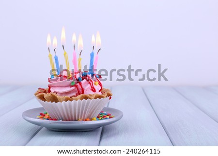 Birthday cup cake with candles on saucer and sparkles on color wooden table and light background
