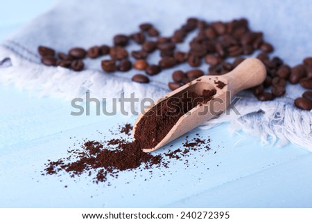 Wooden scoop with ground coffee and beans on jeans material, on blue background
