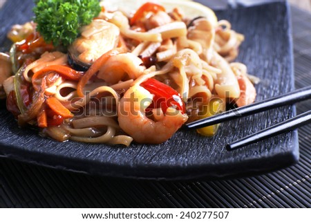 Chinese noodles with vegetables and seafood on plate on bamboo mat background