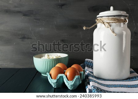 Milk can with bowl of cottage cheese and eggs on wooden table and dark background