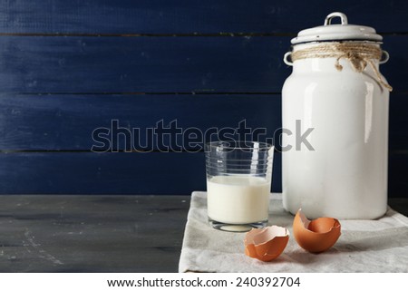 Milk can with glass and eggshell on color wooden background