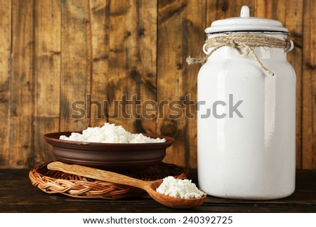 Milk can with bowl of cottage cheese and spoon on rustic wooden background