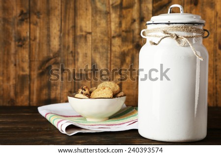 Milk can with bowl of cookies on dishcloth on rustic wooden background