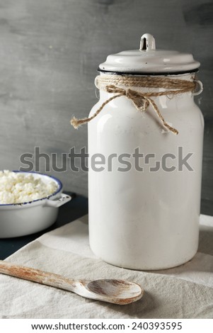 Milk can and cottage cheese with spoon on wooden table and dark background