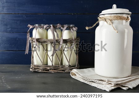 Milk can and glass bottles on color wooden background