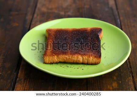 Burnt toast bread on light green plate, on wooden table background
