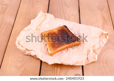 Burnt toasted bread on piece of paper and wooden table background