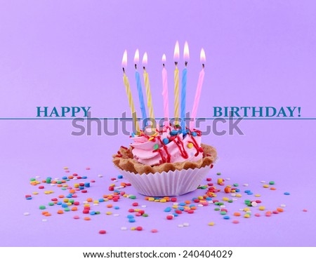 Birthday cup cake with candles and colorful sparkles on purple background