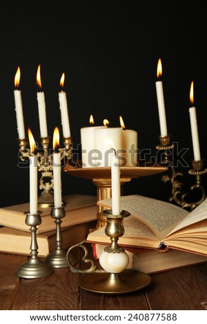 Retro candlesticks with candles and books, on wooden table, on black background