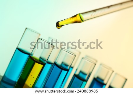 Pipette adding yellow fluid to the one of test-tubes on light background