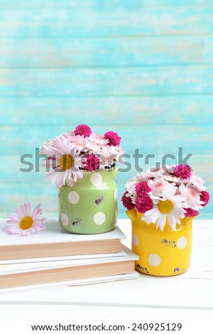 Beautiful flowers in cans on table on light blue background