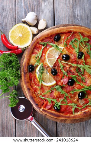 Tasty pizza with spices and round knife on board and wooden table background