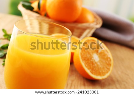 Glass of orange juice and wicker basket with oranges on wooden table and bright background