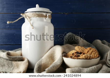 Milk can with plaid and cookies on color wooden background
