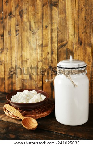 Milk can with bowl of cottage cheese and spoon on rustic wooden background