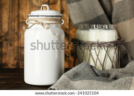 Milk can and glass bottles on rustic wooden background