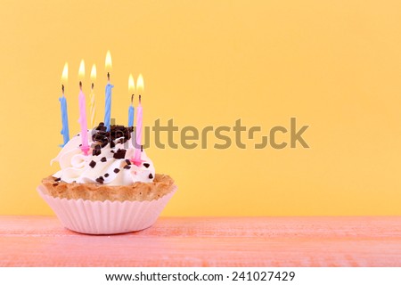 Birthday cup cake with candles on color wooden table and orange background