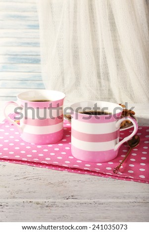 Two mugs of coffee on napkin on table on white curtain background