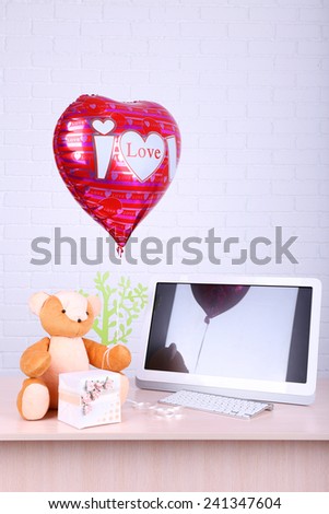 Teddy bear with present box, tree and love heart balloon on wooden  computer table, on the brick wall background