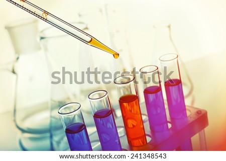 Pipette adding yellow fluid to one of several test-tubes with flasks on light background