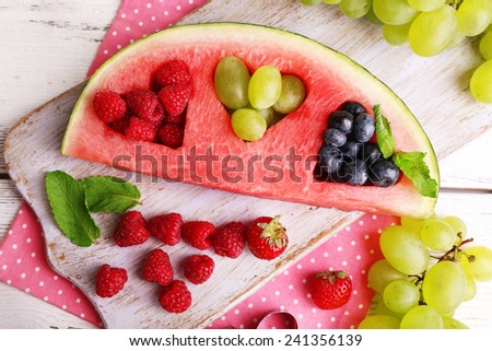 Fresh juicy watermelon slice  with cut out heart shape, filled fresh berries, on cutting board, on wooden background