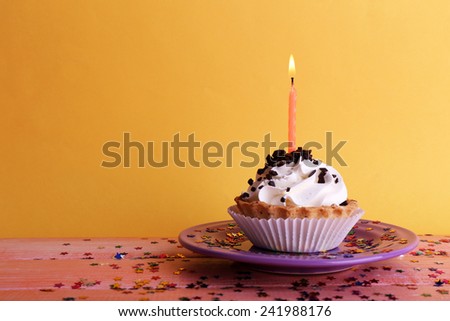 Birthday cup cake with candles on plate on color wooden table and orange background