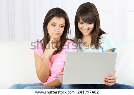 Beautiful girls twins sitting on sofa with notebook