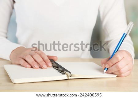 Female hand with pen and notebook at wooden desktop on light background