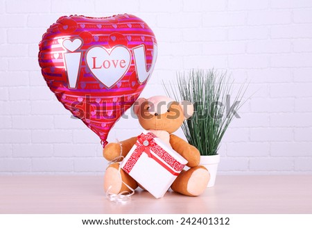 Teddy bear takes gift and love heart balloon with plant on wooden table, on the brick wall background