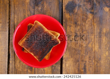 Burnt toast bread on red plate, on wooden table background